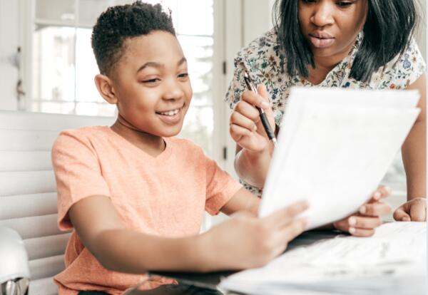 Mother helping son with homework at table.